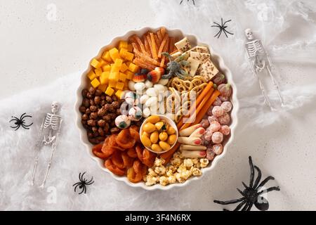 Halloween sweet charcuterie board with pumpkins sweet chocolate candy, spider, crackers on white background. View from above. Stock Photo