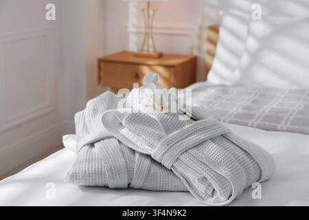 Clean bathrobes with flowers on bed indoors, closeup Stock Photo