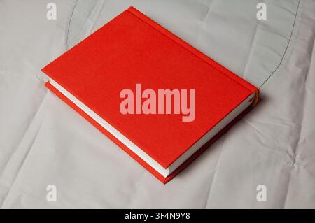 This image features a simple, closed red book with a textured cover, positioned diagonally on a white, slightly rumpled fabric background Stock Photo