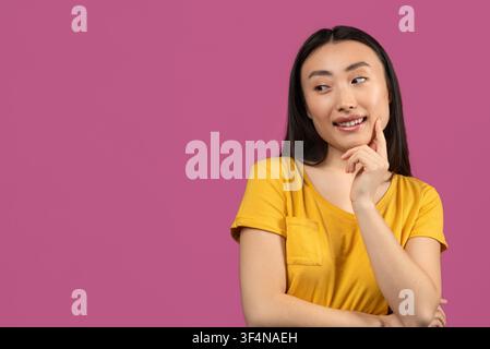 Smiling Asian Woman Wearing Yellow Shirt Thinking, Copy Space For Ideas Stock Photo