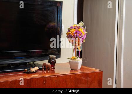 Decorative floral arrangement and small elephant figurine on a wooden cabinet next to a television Stock Photo