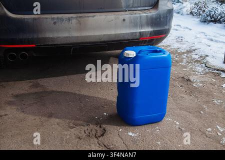 Blue plastic jerrycan next to a dirty car bumper with dual exhaust pipes in winter Stock Photo