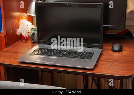 A laptop and computer mouse sit on a wooden desk with a lamp and decorative item Stock Photo