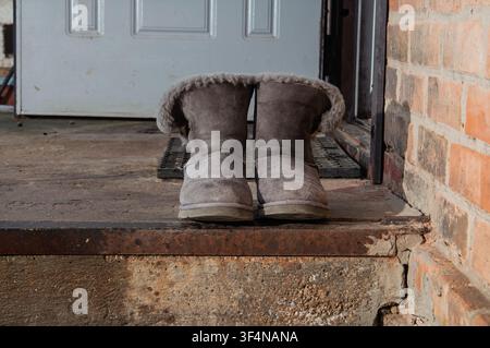 Cozy sheepskin boots left outside on a weathered doorstep near a brick wall Stock Photo