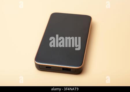 Sleek black portable power bank with gold trim on a neutral beige background Stock Photo