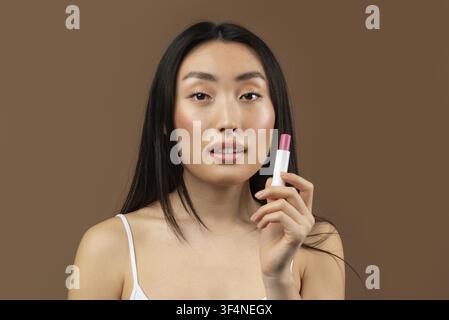 Young Asian Woman Applying Lipstick With Glossy Finish, Happy Expression, Beauty Concept Stock Photo