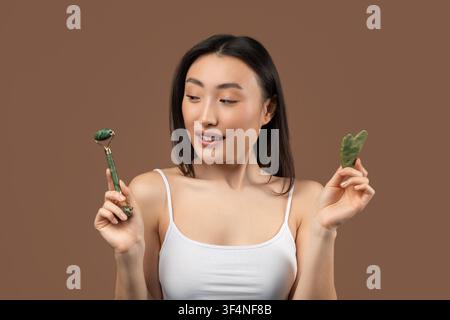 Young Asian Woman Holding Jade Roller And Gua Sha Stone, Skincare Routine Concept Stock Photo