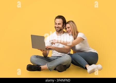 Happy Caucasian Couple Working On Laptop Together, Smiling, Yellow Background Stock Photo