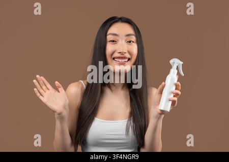 Happy Asian Female Holding Spray Bottle With Hand Up, Smiling, Skincare Concept Stock Photo