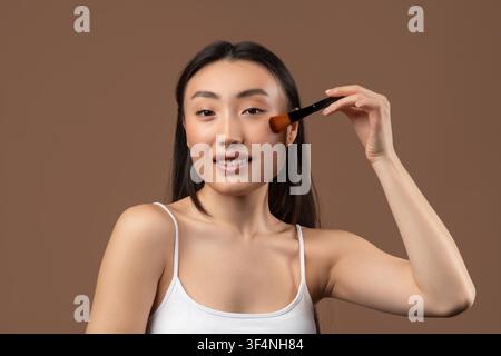 Young Asian Woman Applying Blush On Cheek With Makeup Brush, Beauty Concept Stock Photo