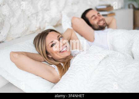Happy Young Woman And Man Smiling Together In Bed, Relaxing At Home Stock Photo