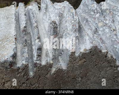 Close-up view of weathered concrete or cement material featuring distinct vertical corrugated ridges and exposed aggregate composition. The rough Stock Photo
