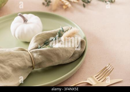 Autumn place setting with sage green plate, linen napkin, dried grasses and golden cutlery on beige background. Copy space. Stock Photo