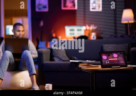 IT professional in an apartment works on cybersecurity with gadgets, tackling hacking attempts, encryption and cyber defense. The screen shows a security breach warning, data security risks. Stock Photo