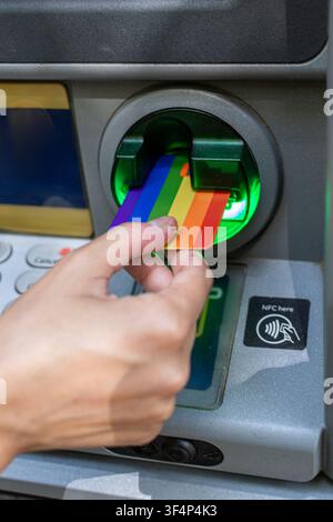 Person inserting rainbow credit card into atm machine Stock Photo