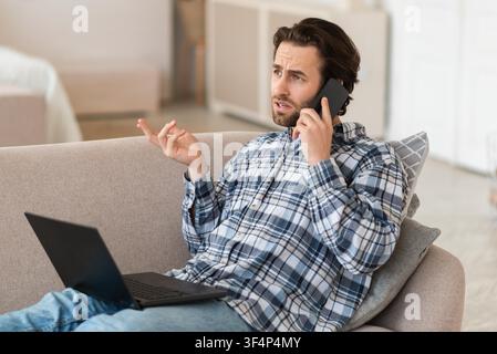 Concerned Caucasian Male Speaking On Phone While Working From Home With Laptop, Business Concept Stock Photo