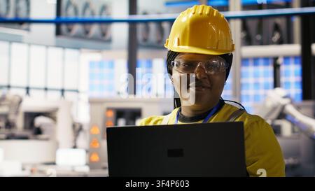 Portrait of smiling solar panels factory engineer analyzing data on laptop to predict gear failures. Happy photovoltaics plant employee using notebook, following maintenance procedures, camera B Stock Photo