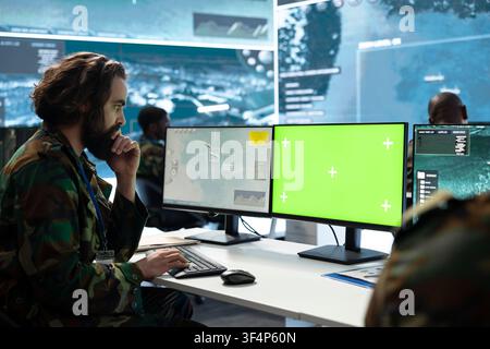 Green screen PC used by military intelligence officer monitoring surveillance displays in warfare command center. Man tracks defensive operation data on chroma key computer in war room Stock Photo