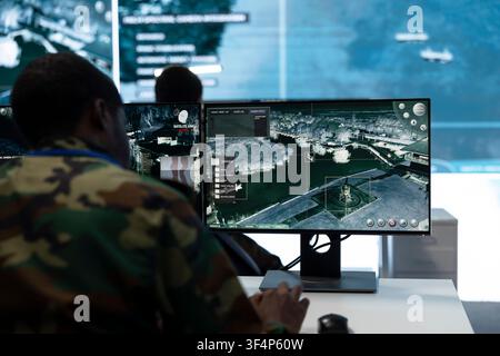 Man in military command post working on PC, looking at surveillance footage on monitor. Military operator watches intelligence feed at workstation desk, close up shot Stock Photo