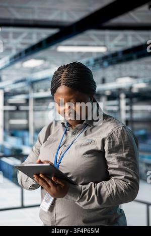 Female programmer in data center using tablet to manage software updates for system stability. African american woman in server room optimizing performance with device, configuring infrastructure Stock Photo