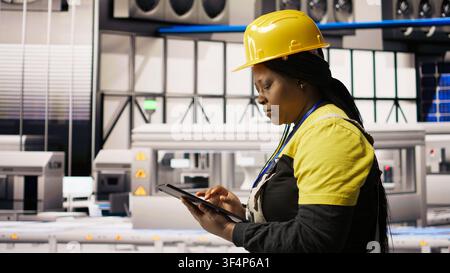 Technician overseeing solar energy installation process, troubleshooting automated machinery, calibrating robotic arms in renewable energy manufacturing facility, camera A Stock Photo