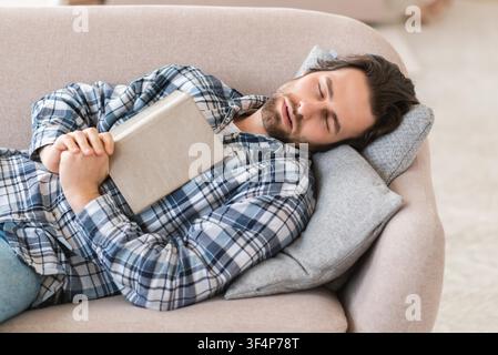 Young Caucasian Man Sleeping On Sofa With Book, Relaxation Concept Stock Photo