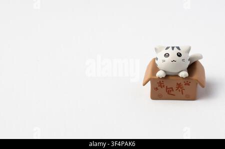 Cute Miniature Cat Figurine Sitting in Small Cardboard Box Stock Photo