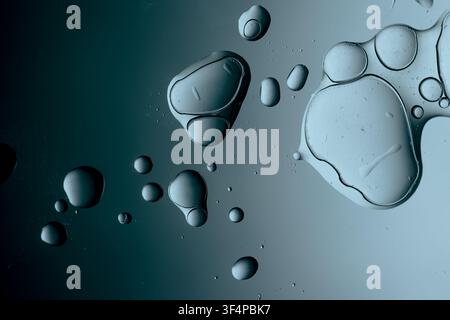 Oil drops creating clear shapes and bubbles on a blue water surface Stock Photo