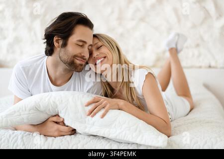 Happy Couple Embracing On Bed, Smiling, Relaxed, Cozy Atmosphere, Romantic Concept Stock Photo