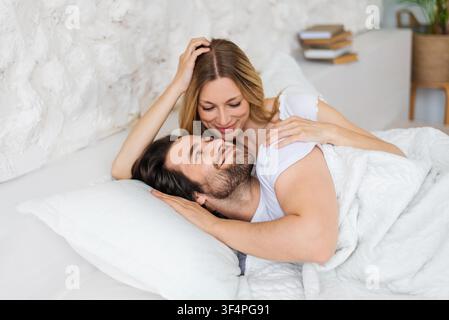 Happy Young Couple Embracing In Bed, Smiling Together, Cozy Morning Stock Photo