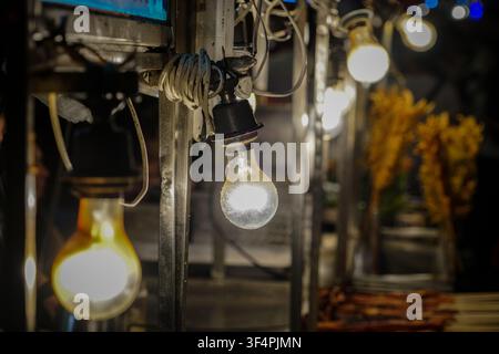 A close-up view shows three incandescent light bulbs hanging from wires on a metal frame, with the central bulb emitting bright white light and a yell Stock Photo