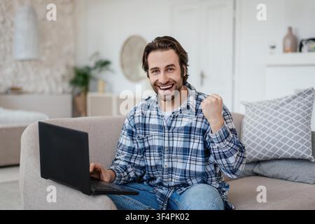Happy Young Man Celebrating Success At Home With Laptop, Casual Attire, Home Office Concept Stock Photo