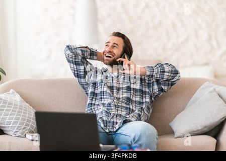 Happy Young Man Talking On Phone While Relaxing At Home, Comfortable Living Room Stock Photo