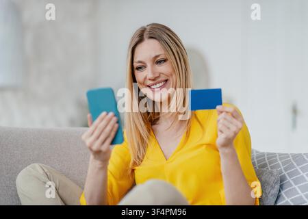 Smiling Caucasian Woman Using Smartphone And Holding Credit Card At Home, Business Concept Stock Photo
