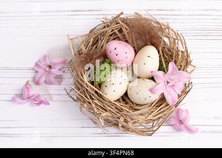 Easter decor on the white wooden table - nest with speckled pink and beige eggs, moss and feathers and sprinkled pink hyacinth flowers around. Stock Photo
