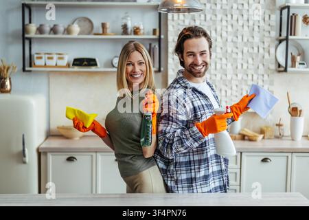 Smiling Young Woman And Man Cleaning Kitchen Together With Cleaning Products And Cloths Stock Photo