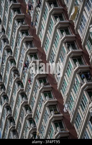 The image shows a brick apartment building facade with rows of light gray, tiered balconies extending outwards in a zigzag pattern, each featuring gre Stock Photo
