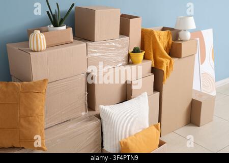 Stacked cardboard boxes and household items for moving or relocation against a blue wall, new home Stock Photo