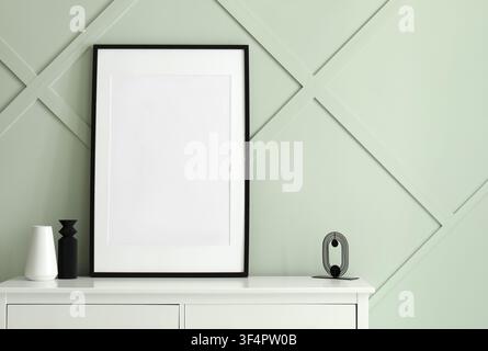 Blank black frame on a white dresser with decorative vases and a modern sculpture against a mint green wall, the wall features a subtle geometric pane Stock Photo