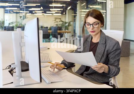 Businesswoman analyzing financial report at computer in modern office workspace Stock Photo