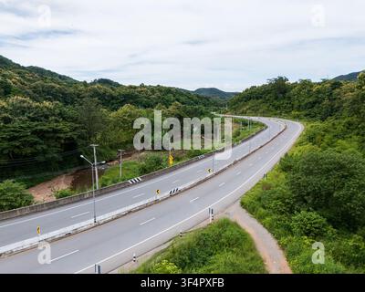 Aerial drone view of Highway 101 winding through lush green mountains between Phrae and Nan, Thailand. A scenic landscape of the road surrounded by tr Stock Photo