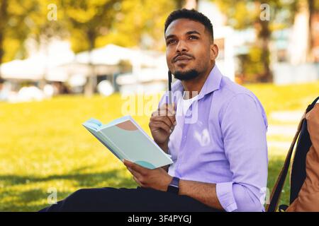 Thoughtful Black Man Writing In Journal While Sitting Outdoors In Park, Relaxing Stock Photo
