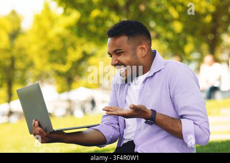 Happy Young Black Man Using Laptop, Laughing And Celebrating In Park, Business Concept Stock Photo