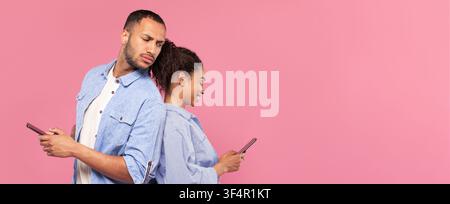 Man And Woman Using Smartphones, Standing Back To Back, Smiling, Pink Background Stock Photo