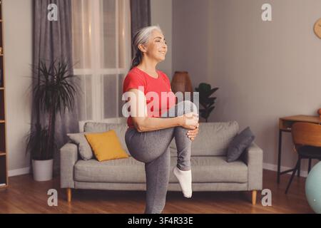 Happy Elderly Caucasian Woman Stretching Leg While Exercising At Home, Wellness Concept Stock Photo