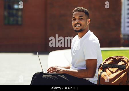 Smiling Black Man Working On Laptop At Outdoor Workspace, Modern Lifestyle Concept Stock Photo