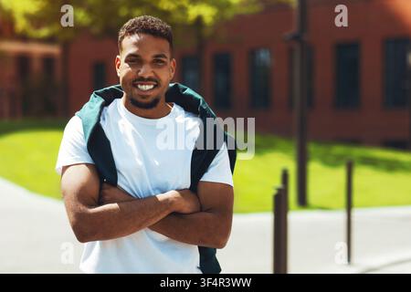 Smiling Young Black Man Standing Outdoors With Arms Crossed, Relaxed Vibe Stock Photo
