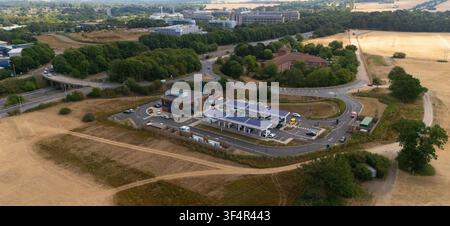 Stevenage, United Kingdom - 16 July 2026: Aerial view of GRIDSERVE Charging Station with solar canopies, electric vehicles at charging points, trees, Stock Photo