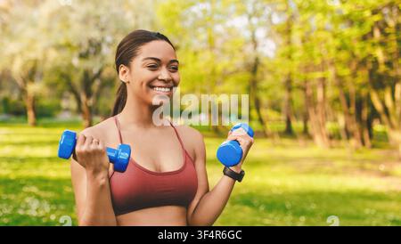 Smiling Young Black Woman Exercising With Dumbbells In Park, Fitness Concept Stock Photo