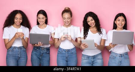 Multiracial Young Women Using Gadgets, Computers And Smartphones, Pink Background Stock Photo